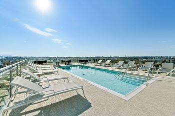 A swimming pool with chaise lounge chairs on top of a building